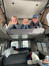 Cozy RV rental interior with three happy kids on the top bunk, enjoying their travel adventure.