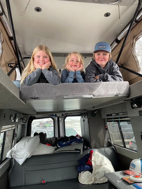 Cozy RV rental interior with three happy kids on the top bunk, enjoying their travel adventure.