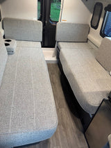 RV rental interior: two grey upholstered benches providing flexible seating and sleeping space, with cup holders and wood floor.