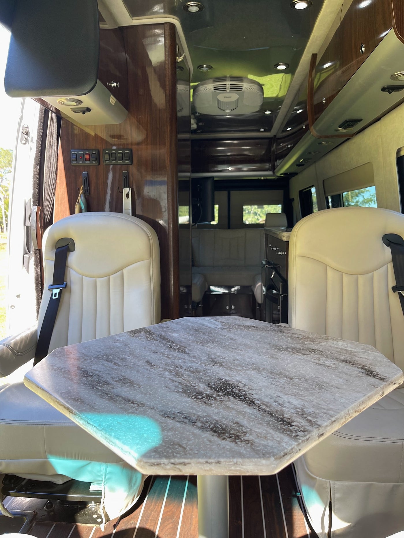 Inside a modern rv rental: dining table, cream leather seats, wood cabinetry, and overhead AC unit for comfortable travel. — photo 7