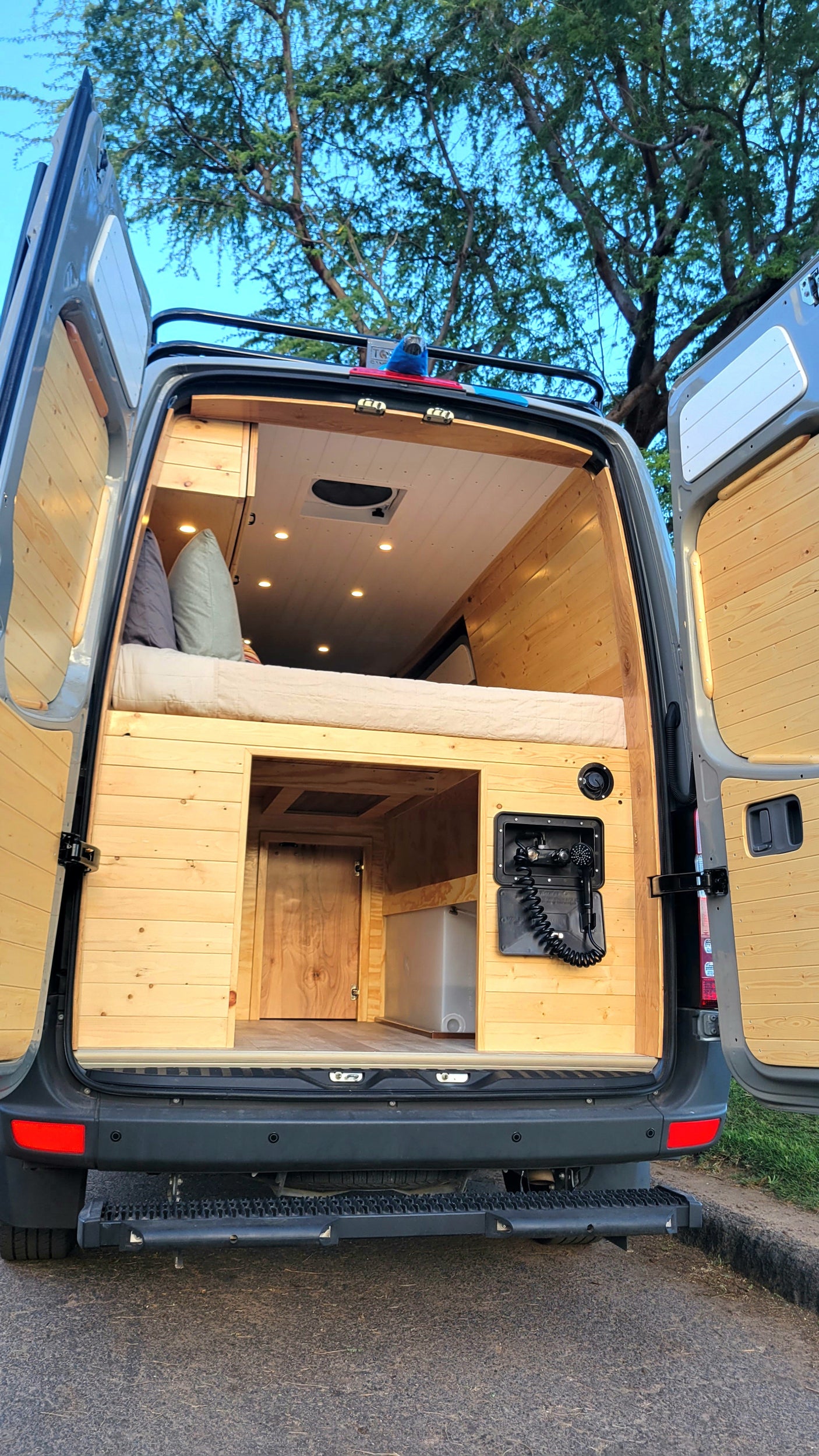 Spacious custom camper van interior, featuring a cozy bed, ample storage, and an outdoor shower. Perfect for an RV rental adventure!