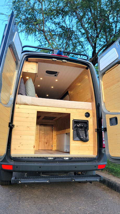Spacious custom camper van interior, featuring a cozy bed, ample storage, and an outdoor shower. Perfect for an RV rental adventure!