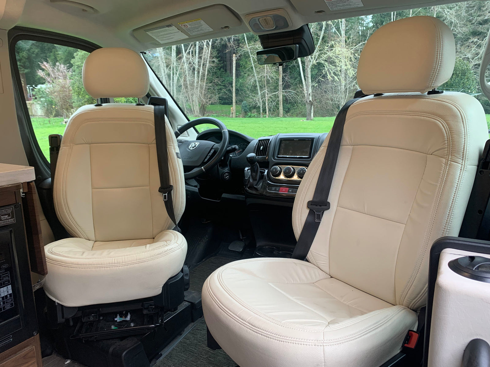 Spacious rv rental interior featuring cream swivel seats, driver's cockpit, and scenic views. Ideal for comfortable travel.