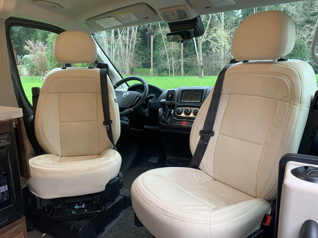Spacious rv rental interior featuring cream swivel seats, driver's cockpit, and scenic views. Ideal for comfortable travel.