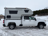 White Chevrolet 2500 HD 4x4 truck with a "FISHHOOK" RV camper, ready for an rv rental winter adventure in the snow.
