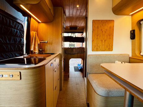 Cozy rv rental interior featuring a compact kitchen, dinette, and bed. Warm wood finishes and efficient design for travel.