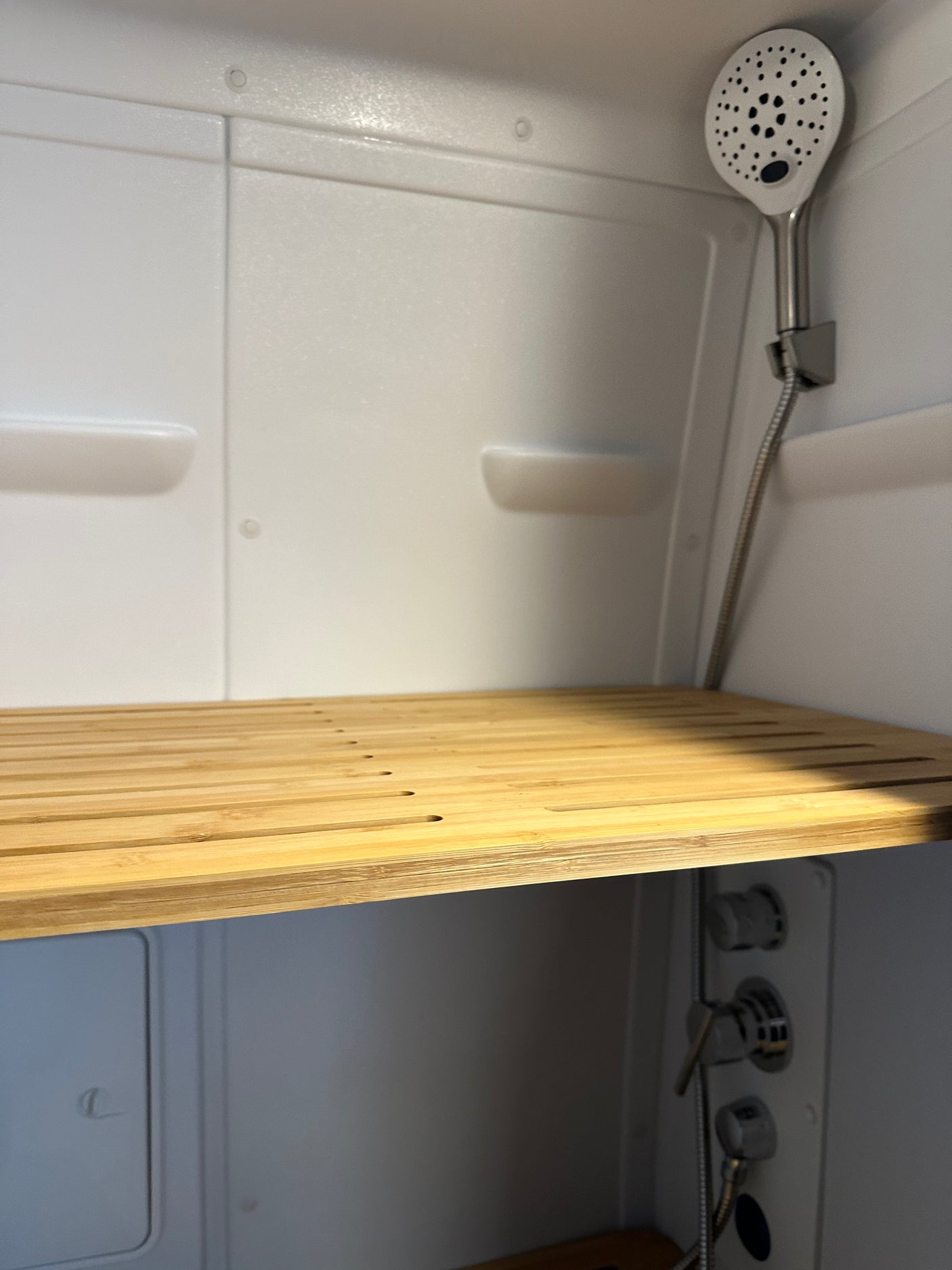 Modern RV rental shower interior features a slatted wood bench, white walls, and a handheld shower.