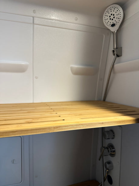 Modern RV rental shower interior features a slatted wood bench, white walls, and a handheld shower.
