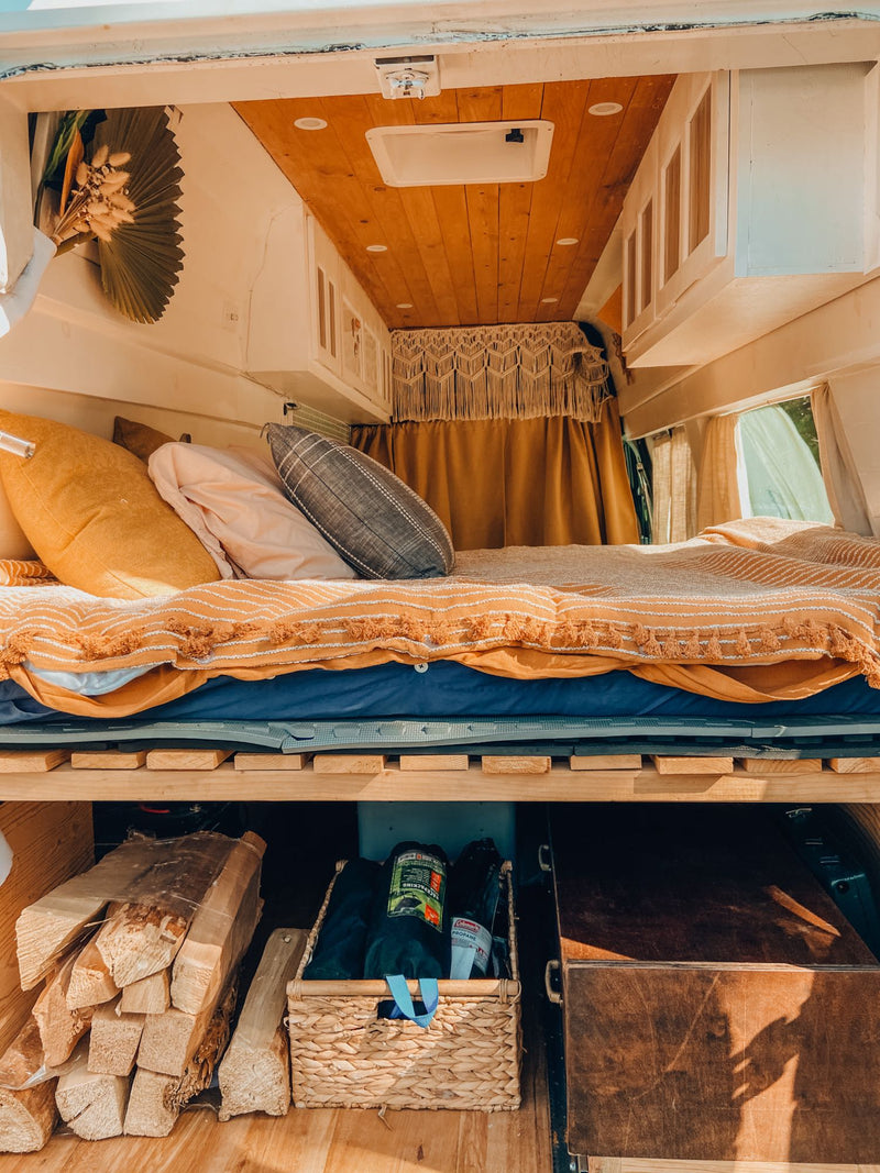 Cozy RV rental interior showcasing a comfortable bed, overhead cabinets, and clever under-bed storage with firewood. — photo 15