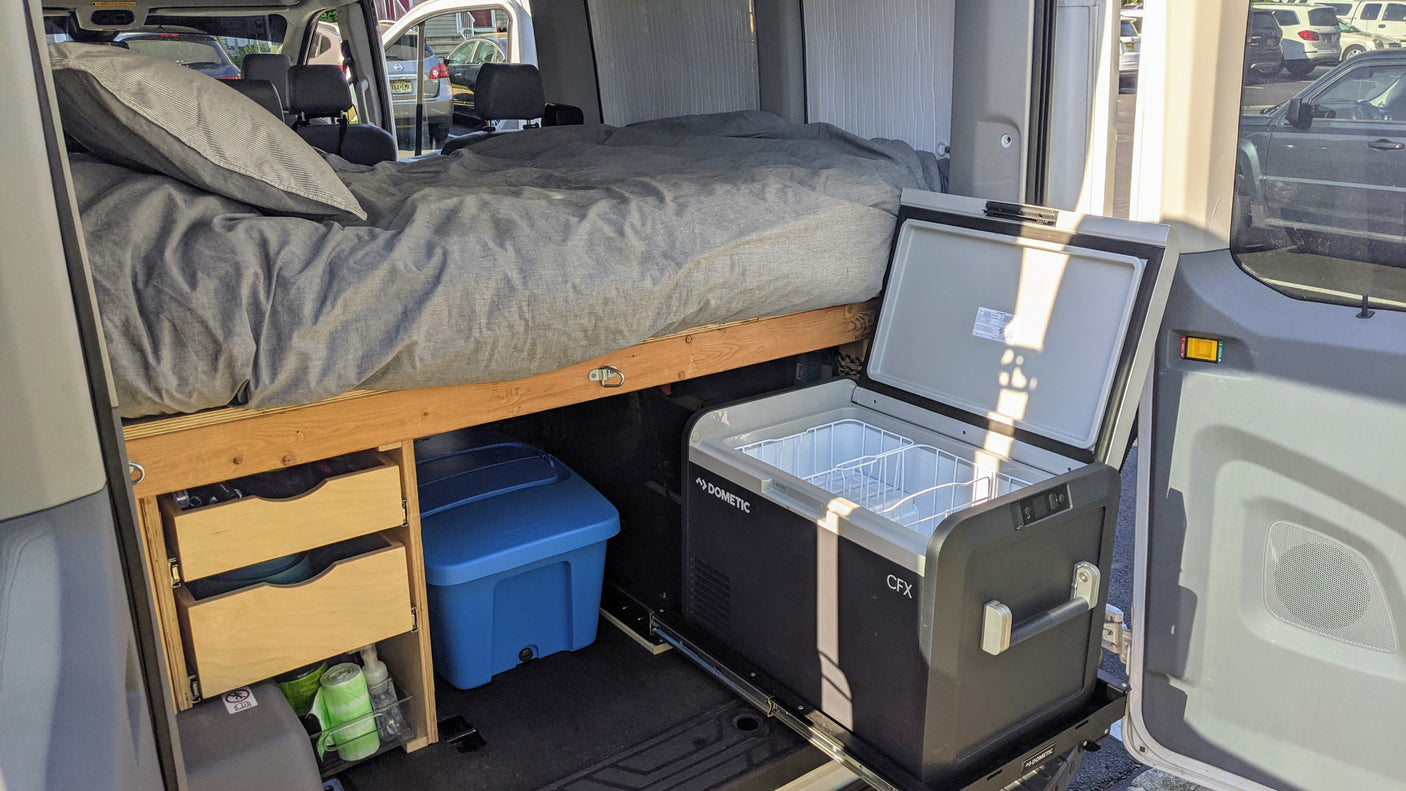 Compact rv rental layout: comfy bed, storage drawers, & Dometic cooler on a slide, ready for van life.