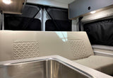 RV rental interior: light-colored bench with quilted design, stainless sink, and overhead storage for comfortable travel.