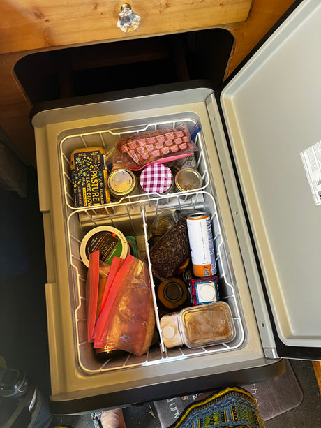 This rv rental fridge is well-stocked with food: Trader Joe's eggs, sauces, drinks, and jars, neatly organized for a trip.