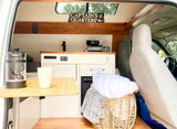 Cozy RV rental interior with kitchenette, dining area, and bedding. A "Captain's Quarters" sign adds nautical charm.