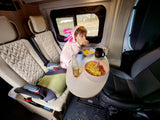 Child in a pink axolotl robe eats breakfast at a table in an RV rental, a cozy scene for family travels.