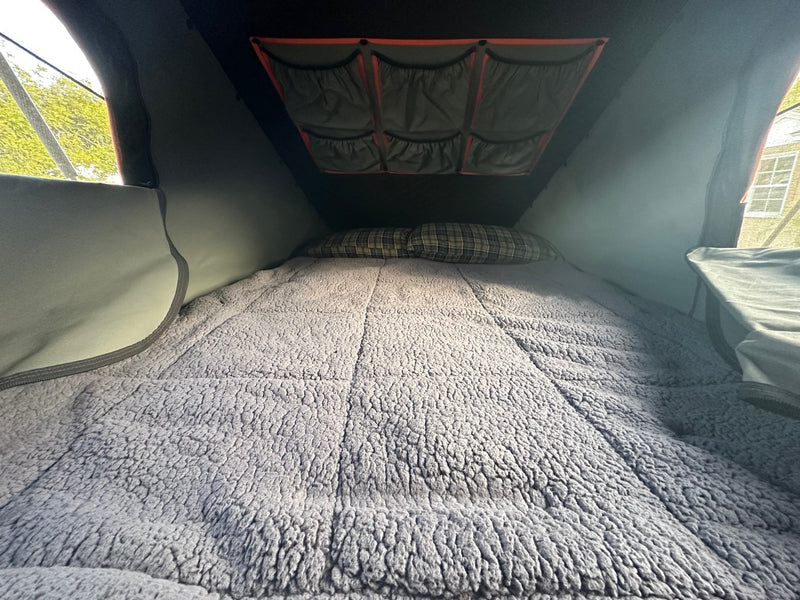 An RV rental's comfy interior: a bed with a plush blanket & plaid pillows, and ceiling storage pockets visible. — photo 15