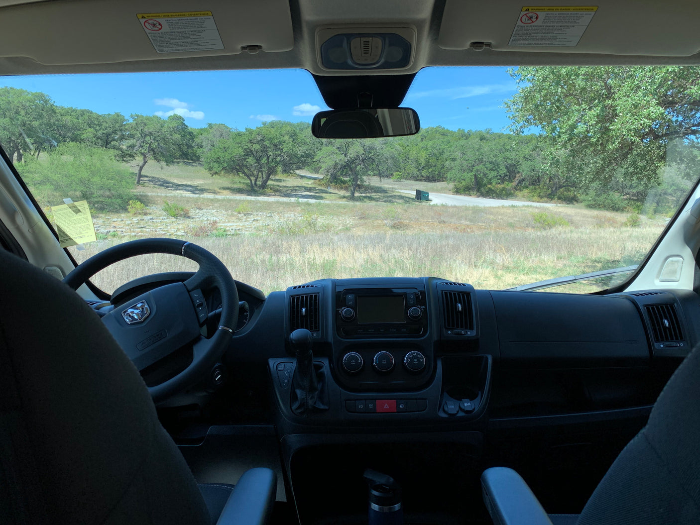 Interior of an RV rental, with a view of its dashboard and a sunny landscape of trees and a road.