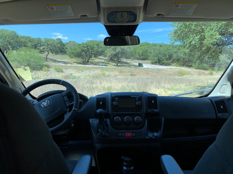 Interior of an RV rental, with a view of its dashboard and a sunny landscape of trees and a road.
