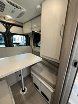 RV rental interior: light wood dinette with bench seating, overhead storage, and ceiling AC unit. Cozy and functional.