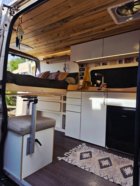 Cozy RV rental interior with a bed, kitchen, fridge, dining table, wooden ceiling, and rug for comfortable travel.
