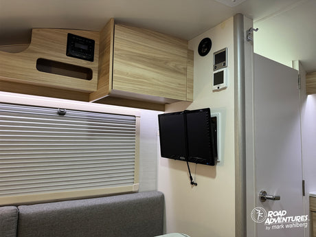 Experience comfort in this RV rental with a wall-mounted TV, wood cabinets, control panel, and adjustable window blinds.