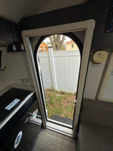 Inside an rv rental: an open door reveals a backyard scene with a fence, next to a Dometic cooler and seating.