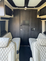 Plush rv rental interior with white quilted leather seats, dark wood walls, overhead storage, and LED lighting. Ideal for travel.