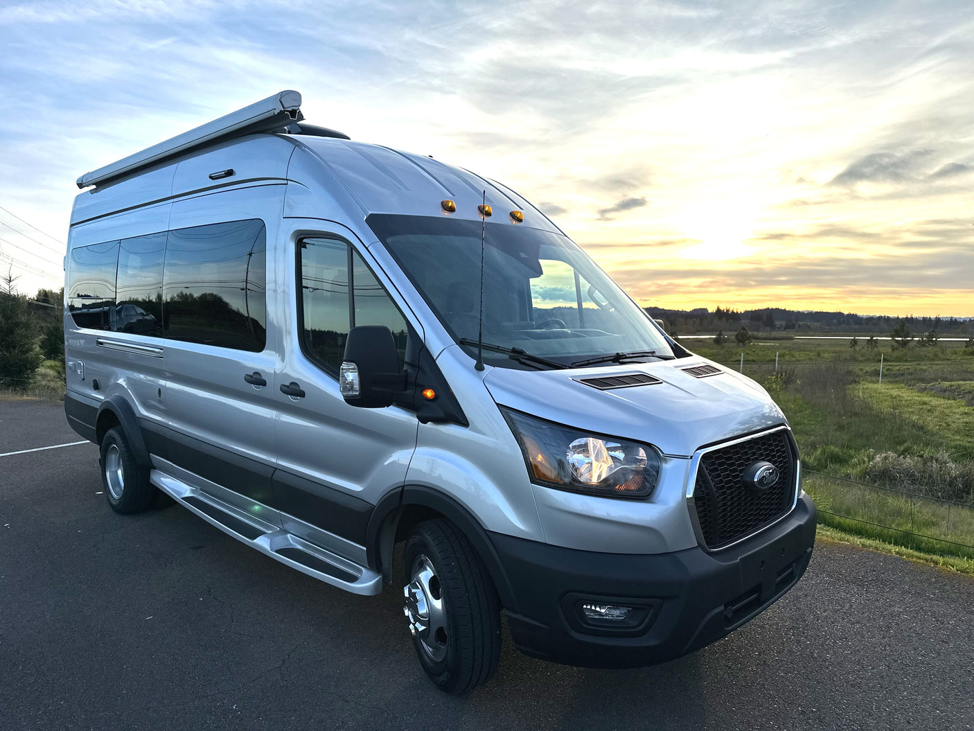 Silver Ford Transit camper van, perfect for RV rental, parked at golden hour with rural landscape.