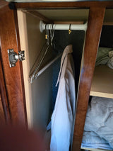 RV rental closet: view inside a small wardrobe with a tension rod, hangers, a jacket, and shelved storage for bedding. Compact & functional.