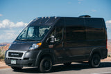 Dark gray Ram ProMaster camper van, an RV rental, parked in a scenic desert. Colorado plate BRX-C40.
