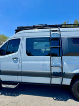 Side view of a light blue RV rental featuring a ROOFNEST roof rack, ladder, and side steps, ready for adventure.