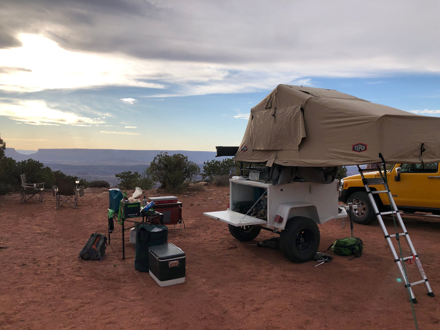 Overland camping with an RV rental setup: rooftop tent on a trailer & yellow SUV overlooks a vast canyon. Ideal outdoor adventure.