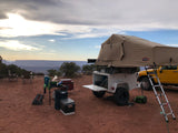 Overland camping with an RV rental setup: rooftop tent on a trailer & yellow SUV overlooks a vast canyon. Ideal outdoor adventure.