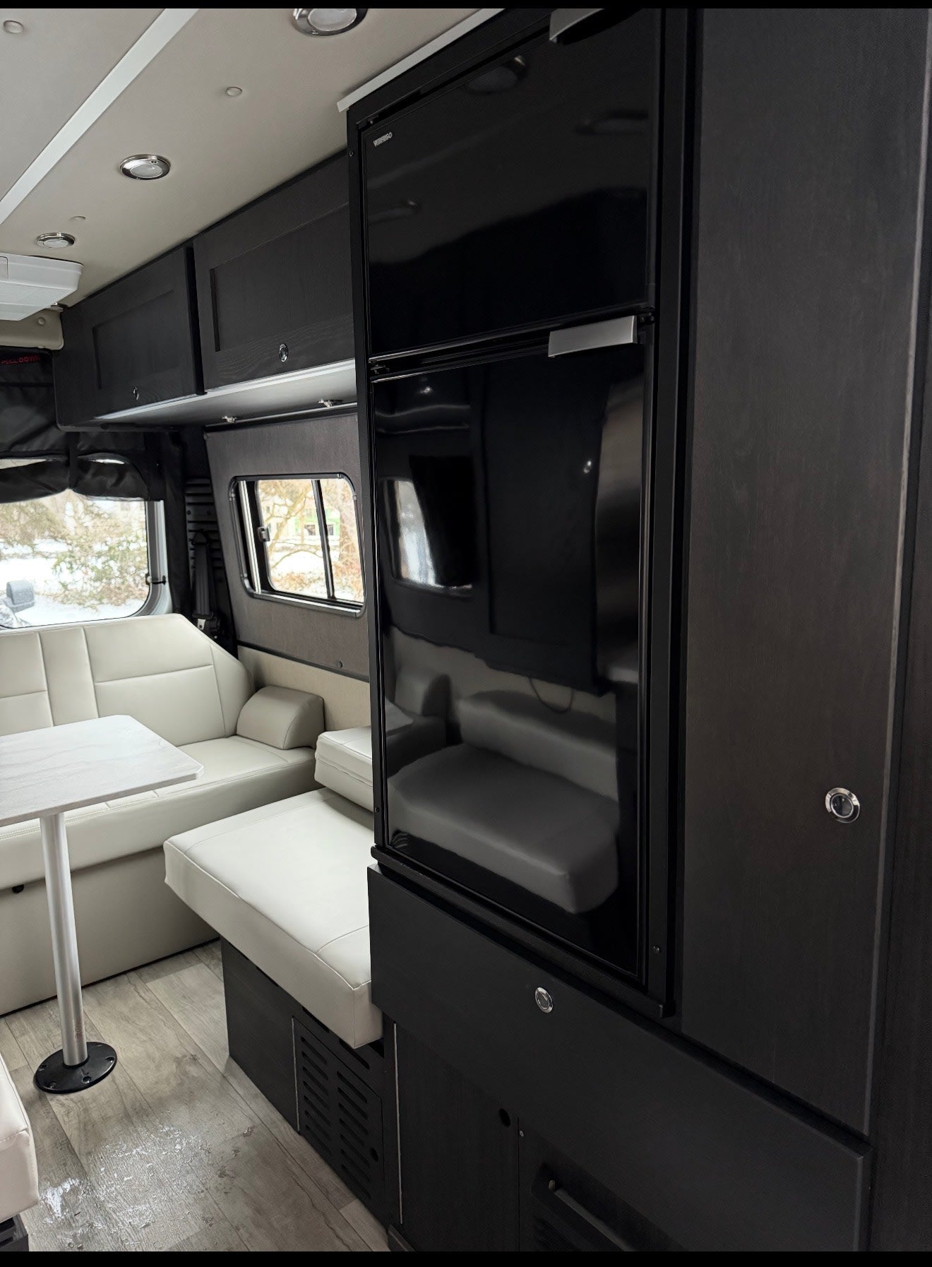 This RV rental showcases a modern interior with a black refrigerator, white dinette seating, and dark cabinetry. Ideal for travel. — photo 13