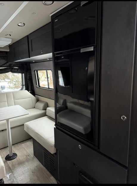 This RV rental showcases a modern interior with a black refrigerator, white dinette seating, and dark cabinetry. Ideal for travel.