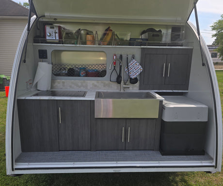Explore this compact outdoor kitchen in an RV rental, featuring a sink, cooktop, and organized storage for easy camping meals.