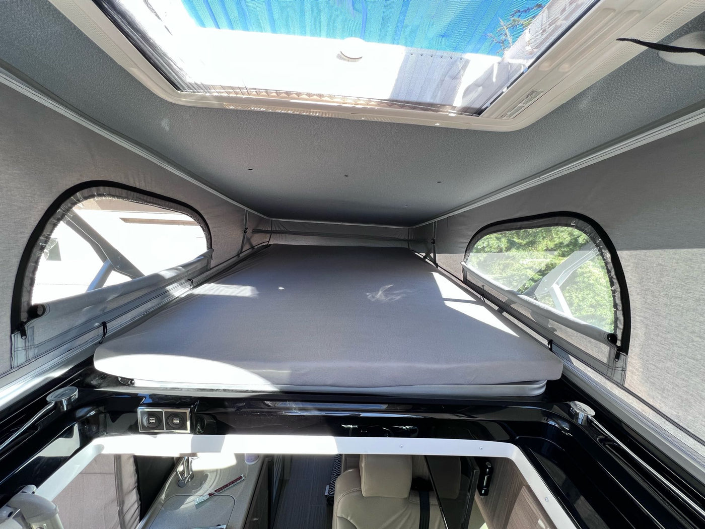 RV rental interior: A raised bed platform, overhead skylight with blue mesh, and side windows in a pop-top camper. — photo 15