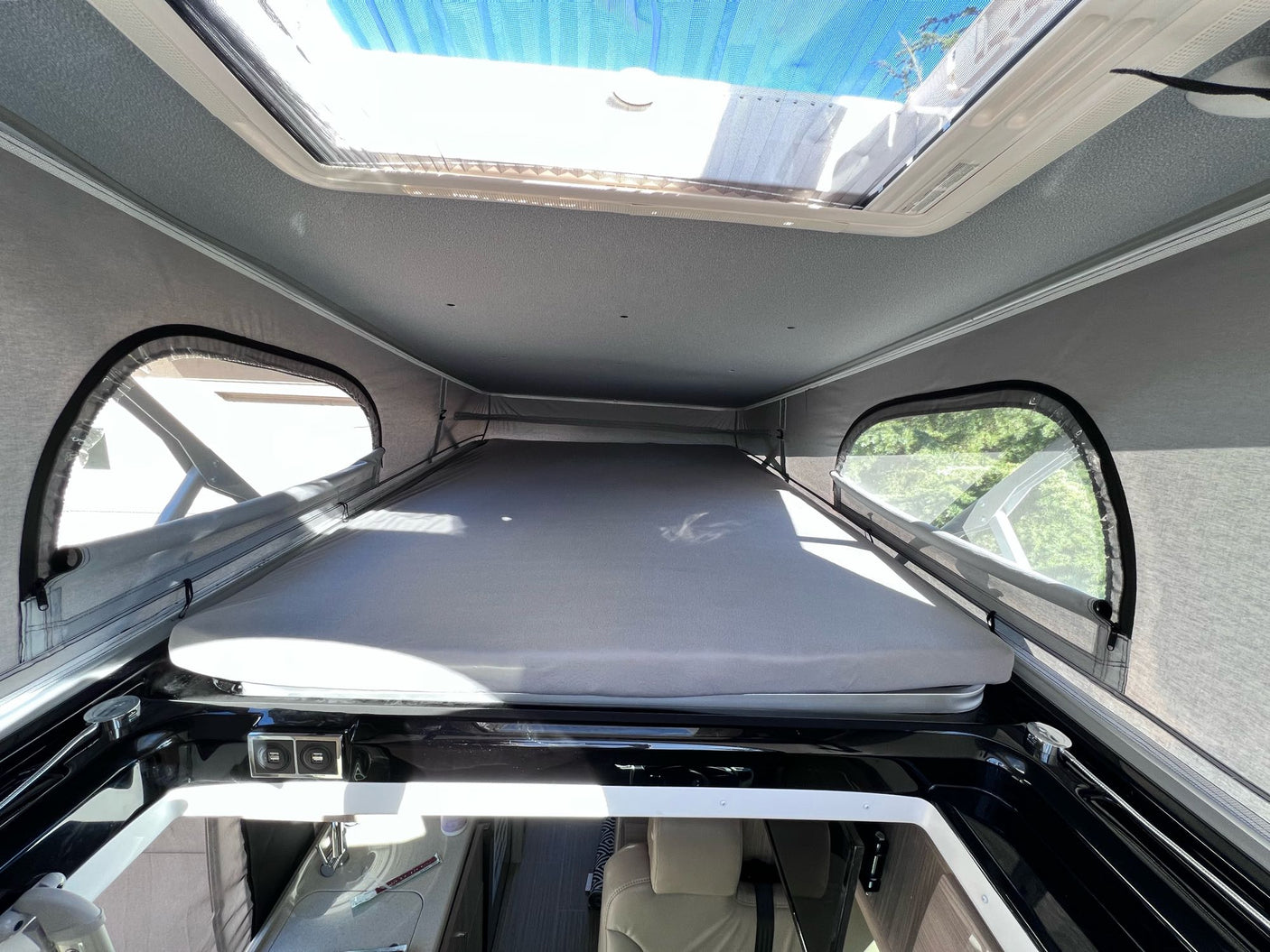 RV rental interior: A raised bed platform, overhead skylight with blue mesh, and side windows in a pop-top camper.