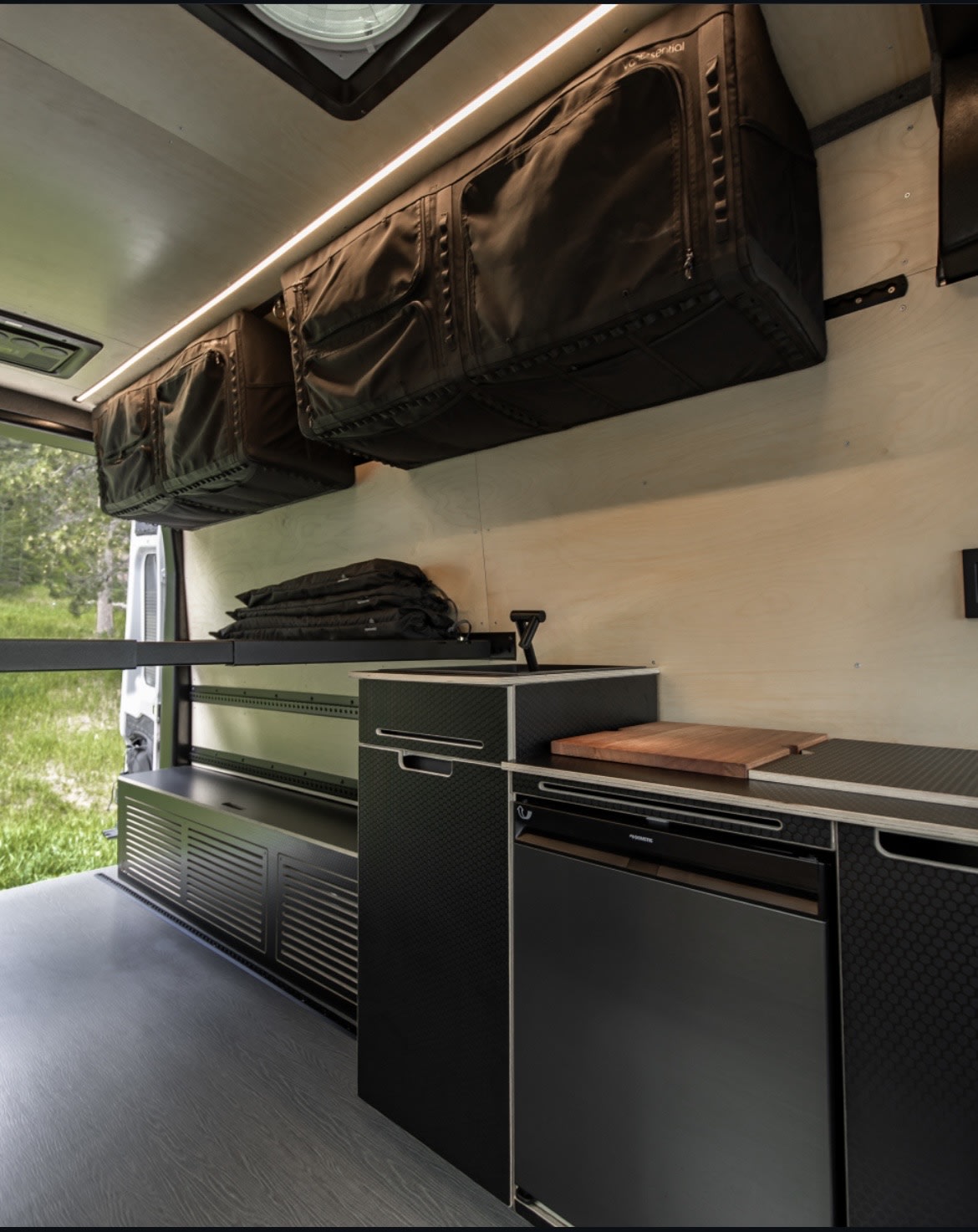 Sleek RV rental van interior: custom kitchen, fridge, and clever overhead storage for efficient travel setups.
