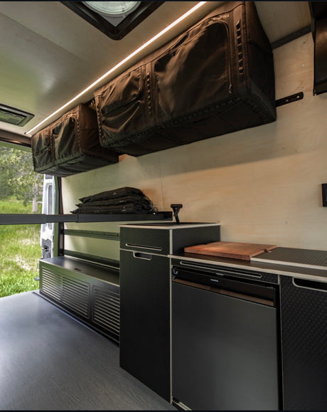 Sleek RV rental van interior: custom kitchen, fridge, and clever overhead storage for efficient travel setups.