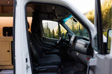 This RV rental showcases its cabin & kitchenette, with a driver's perspective of scenic mountains & a vibrant forest outside.