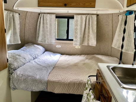 Cozy rv rental interior: comfortable bed with floral and quilted bedding, windows with curtains, and a compact sink.