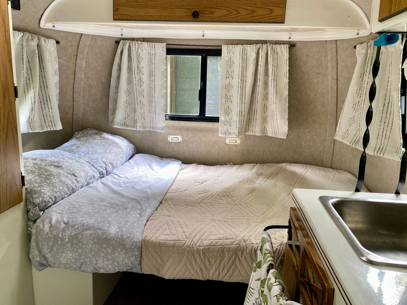 Cozy rv rental interior: comfortable bed with floral and quilted bedding, windows with curtains, and a compact sink. — photo 8