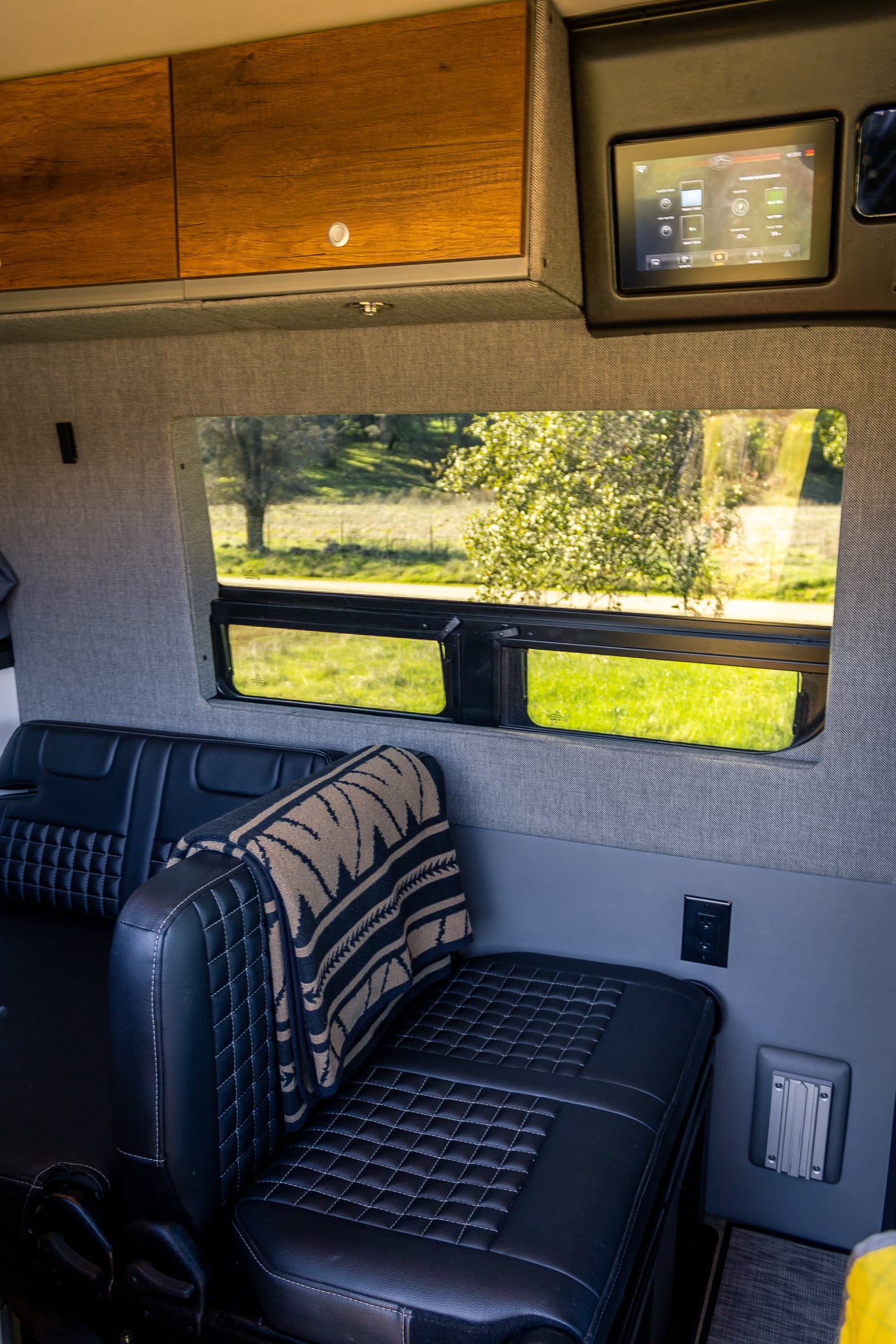 Inside a premium rv rental van: black quilted seats, wooden cabinets, and digital controls. View of nature through window.