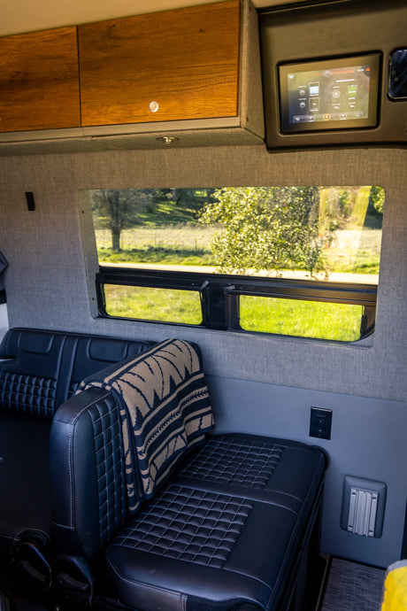 Inside a premium rv rental van: black quilted seats, wooden cabinets, and digital controls. View of nature through window.