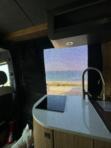 Modern RV rental kitchen with an ocean view through the window screen, a dog, and sleek counter space.