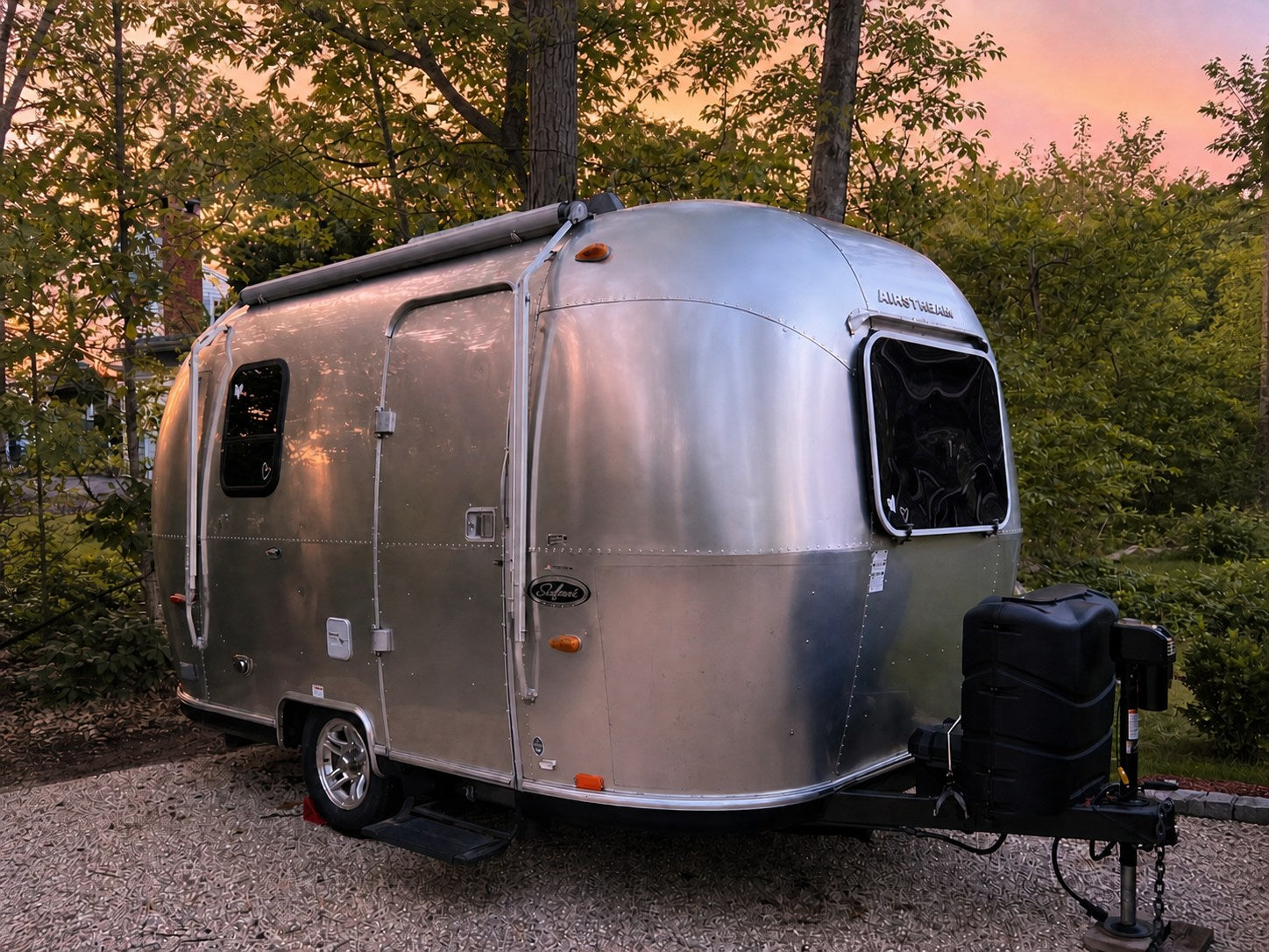  parked on a driveway near trees. Ready for adventure!|A silver Airstream RV rental glows under a colorful sunset