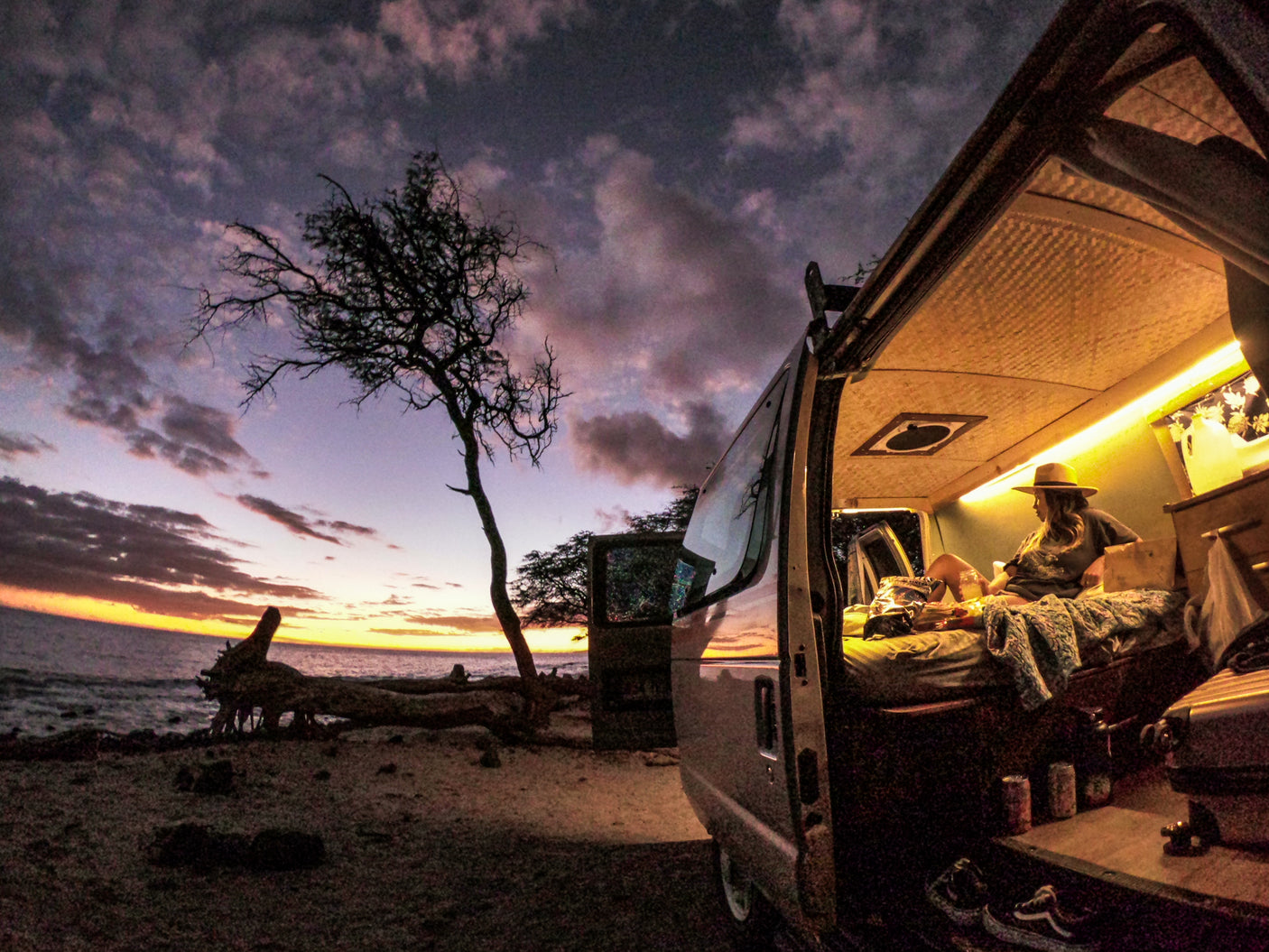 A person relaxes inside a cozy RV rental camper van at sunset, parked seaside for a serene travel experience.