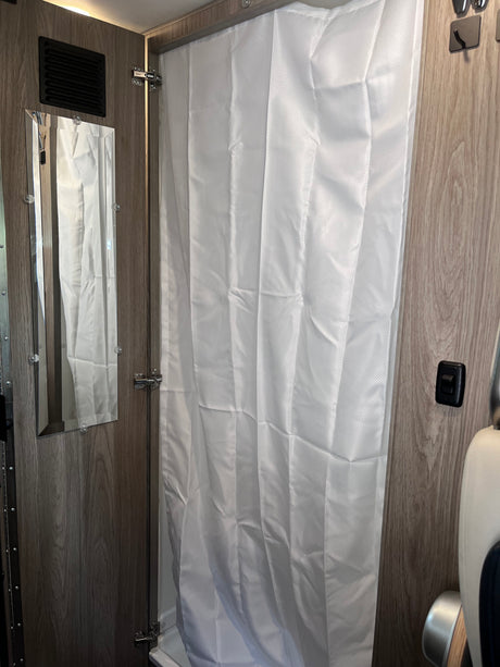 RV rental interior: a compact shower area with white textured curtain, wall-mounted mirror, and wood-look walls.