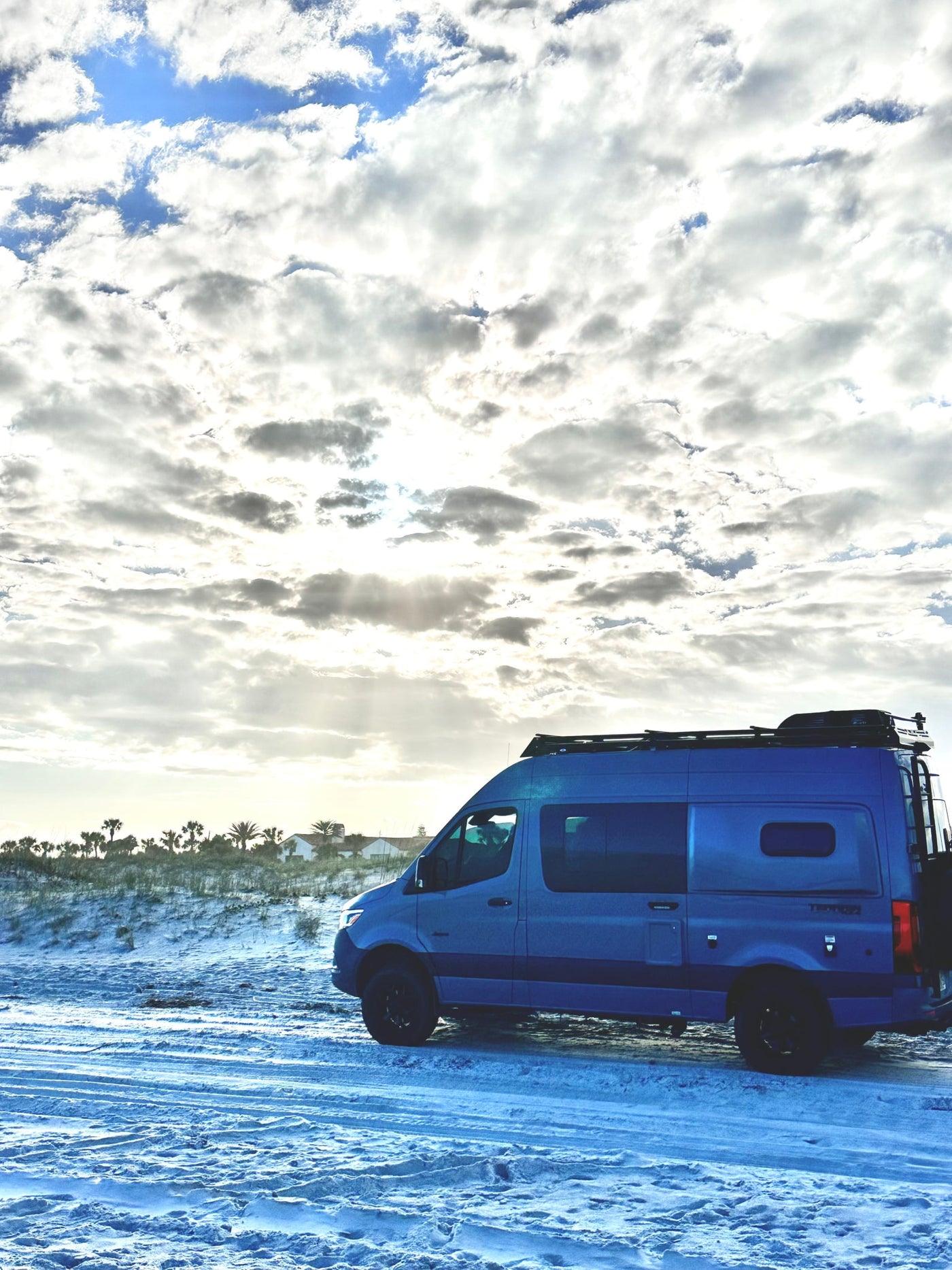  surrounded by green trees and snow.|Blue RV rental camper van parked on a bright sandy beach with palm trees — photo 2
