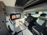Bright RV rental interior featuring a dinette with cream seats and a table, plus front cabin seats and overhead storage.
